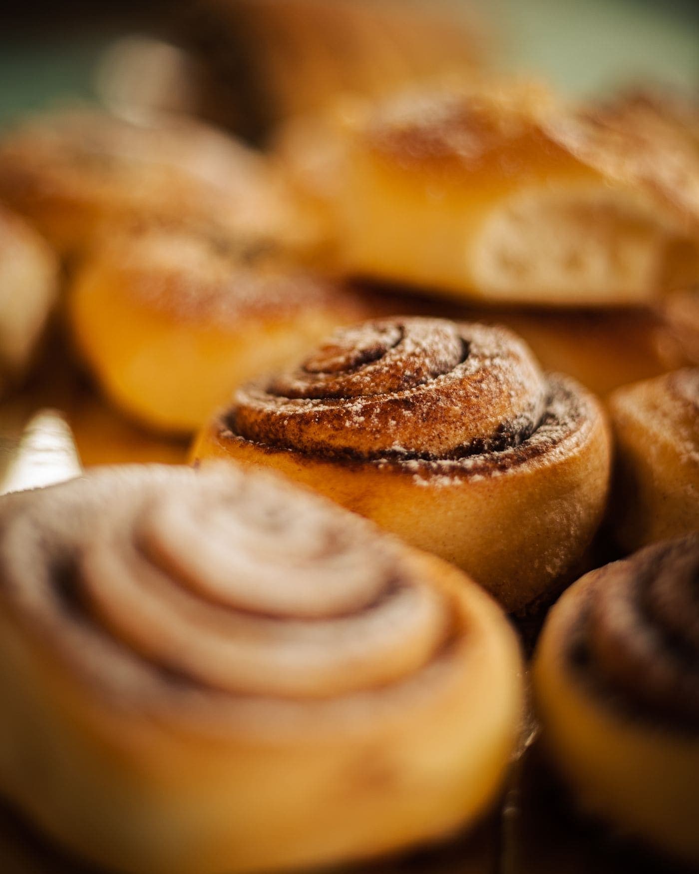 A tray of freshly baked spiral cardamom buns, glossy and golden, shot close up.