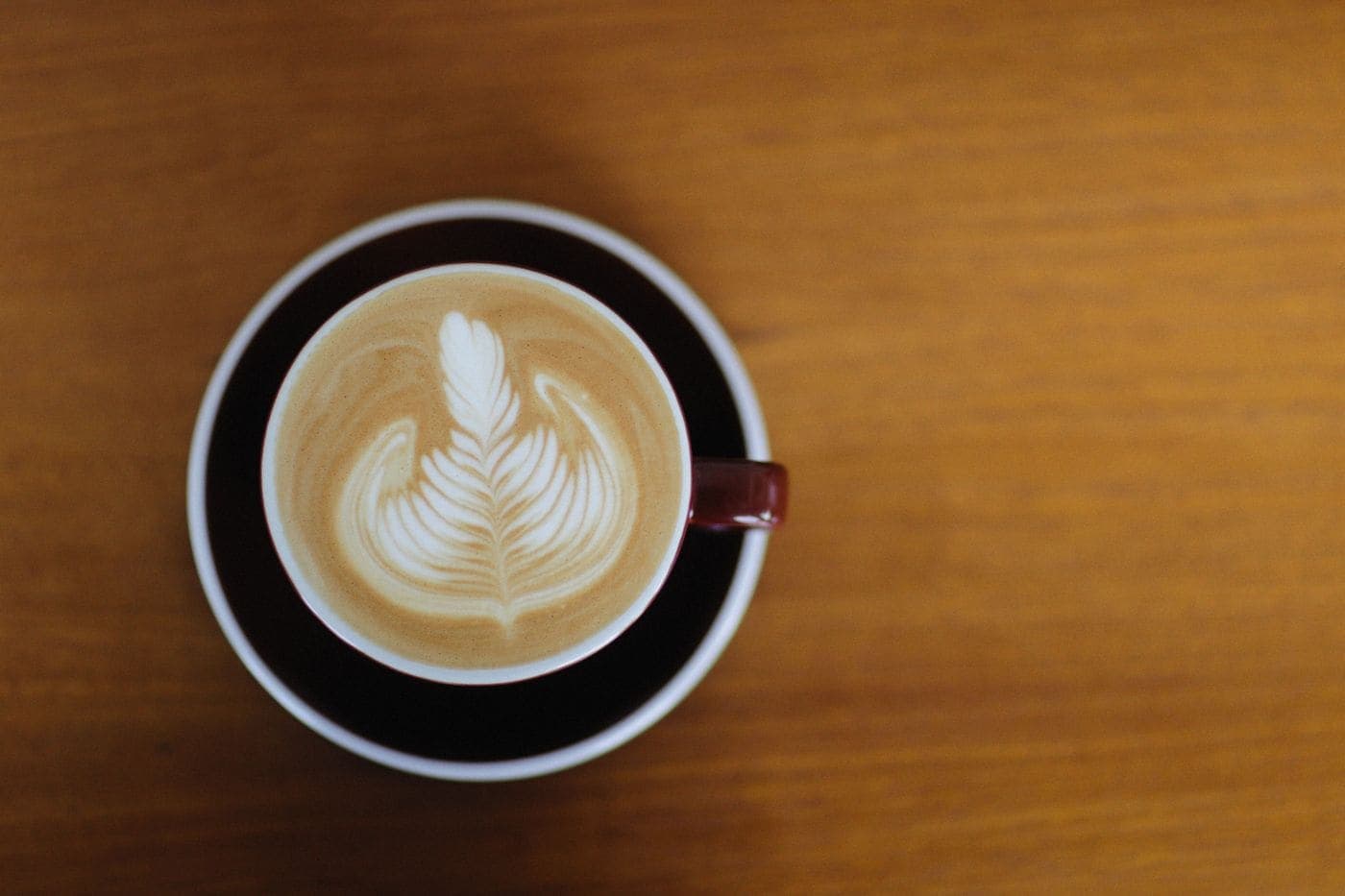A latte seen from above, with a rosetta poured into the microfoam, in a dark cup on a wooden table.