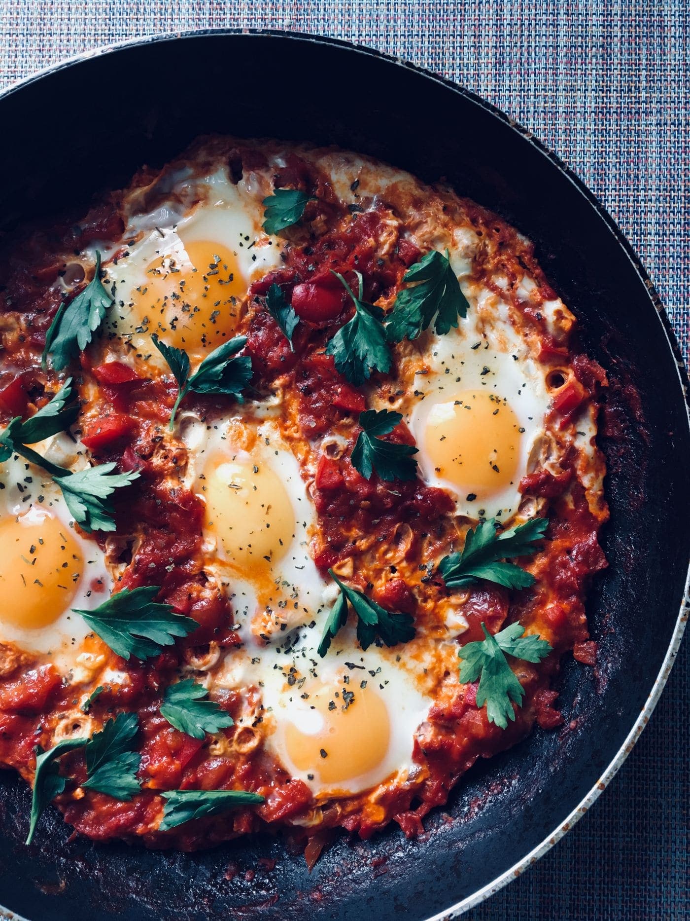 Shakshuka in a cast-iron pan: eggs baked into a rich tomato sauce and scattered with parsley.