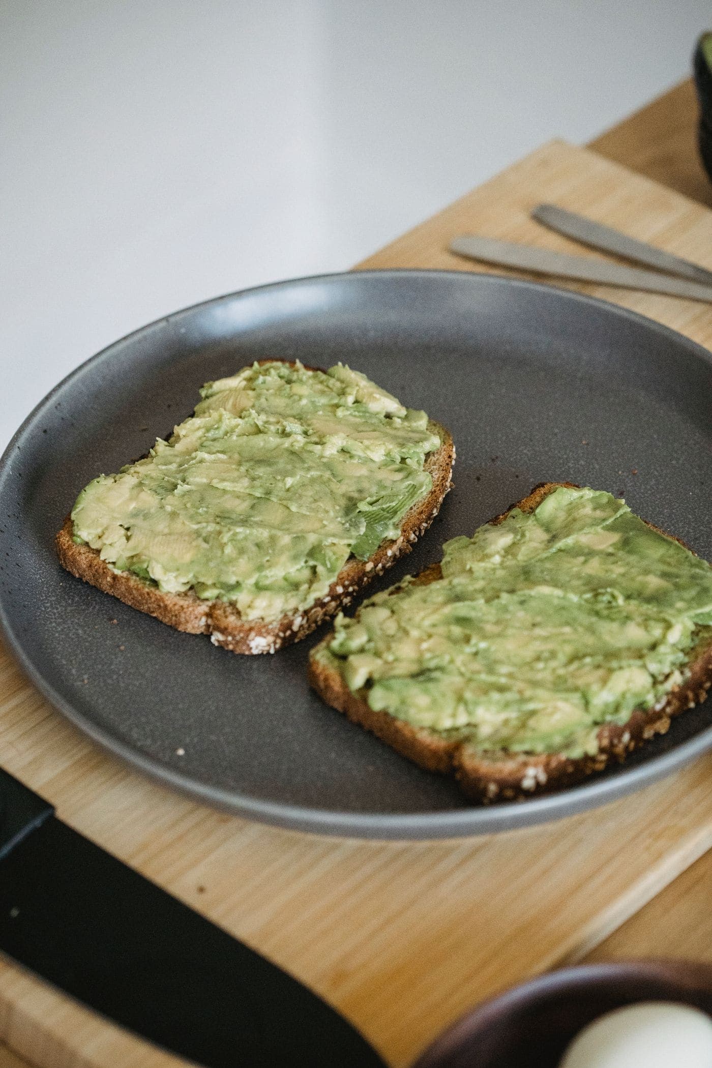 Two slices of smashed avocado on toasted sourdough, served on a matte dark ceramic plate.