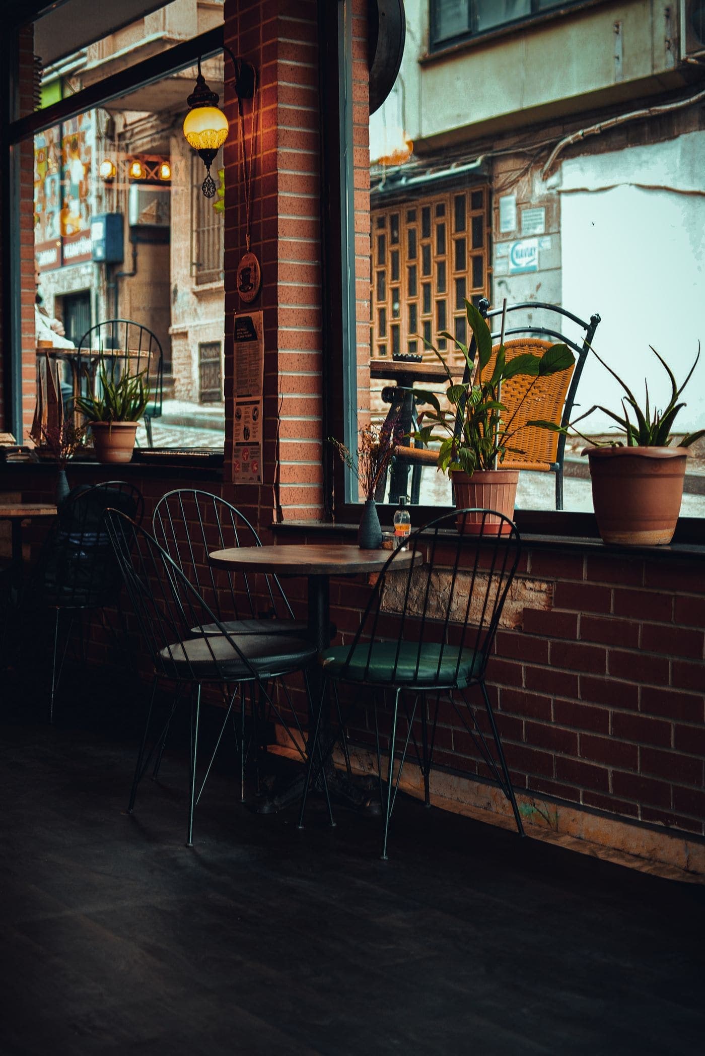 The back corner: exposed brick, bistro chairs and a row of potted plants along the windowsill.