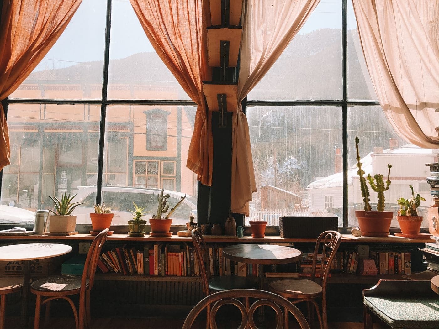 The front window on a bright morning: bentwood chairs, small potted plants on the sill and warm light through linen curtains.
